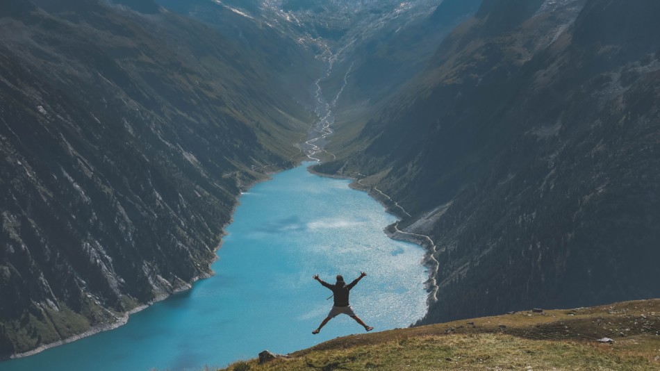 Man jumping on a mountain overlooking a large river basin